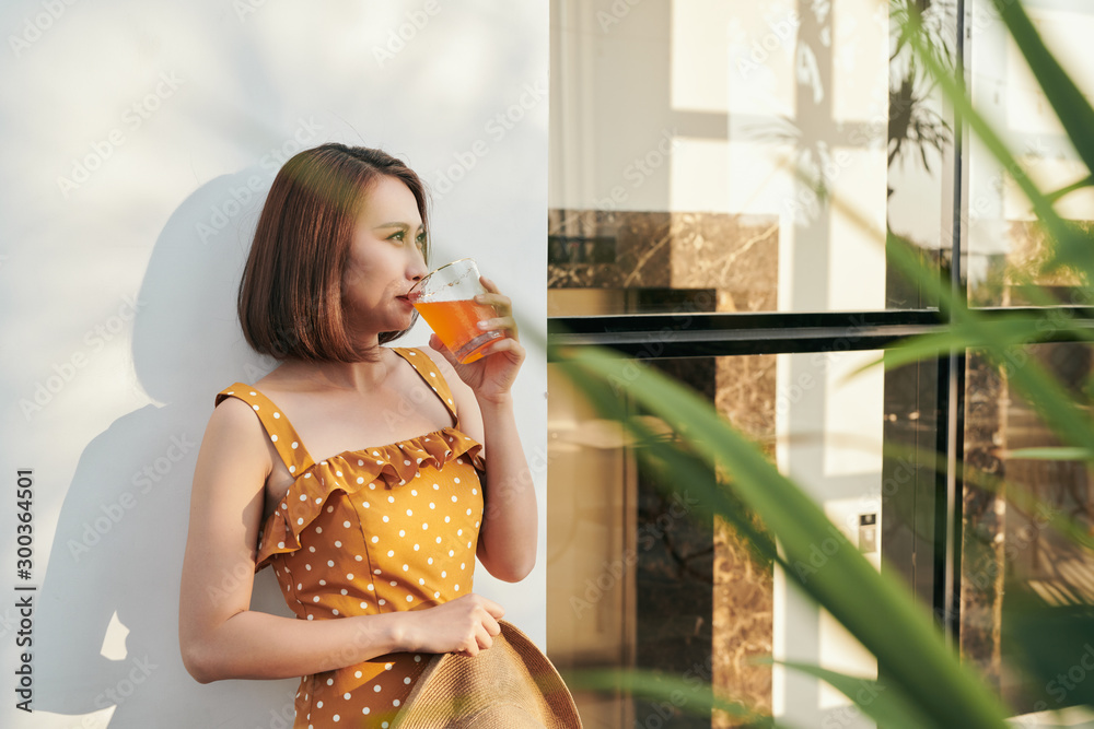 Happy summer woman enjoying orange juice behind the wall