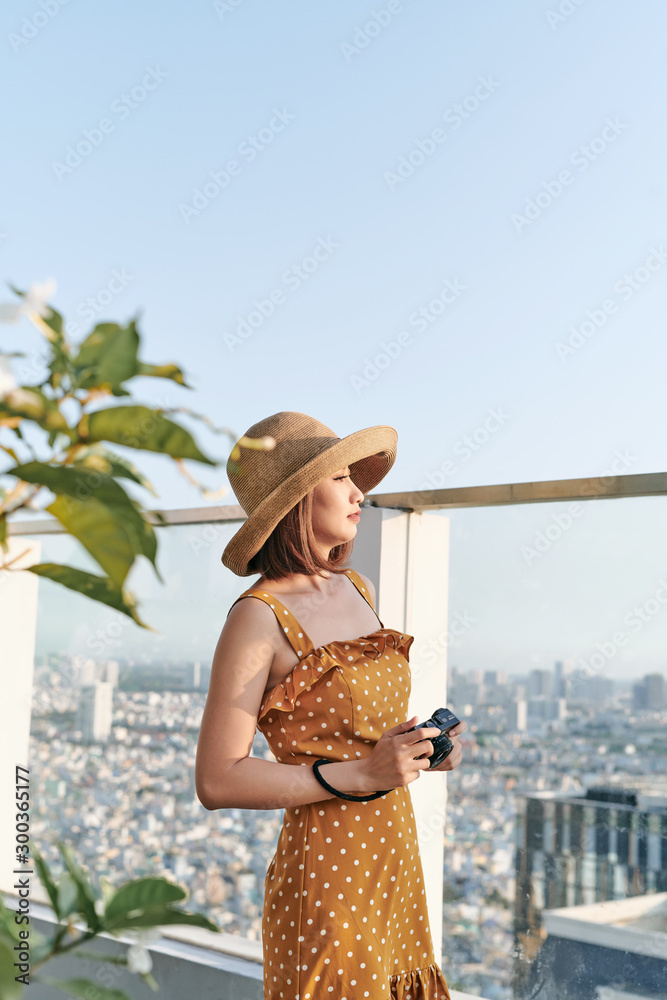 年轻的亚洲女孩站在屋顶上，用相机拍照。夏天的概念。