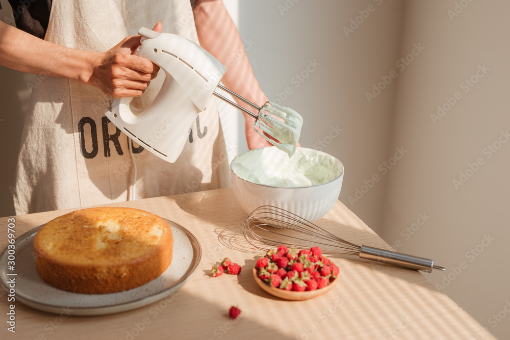 Male hands whipping whites cream in glass bowl with mixer on wooden table. Making sponge cake or red