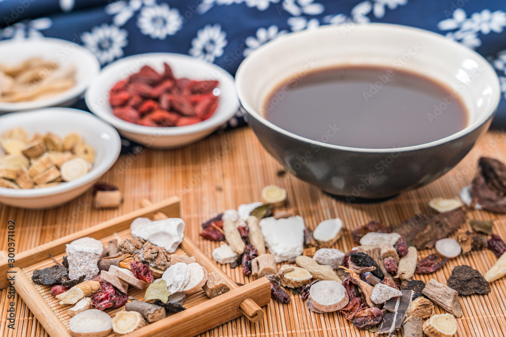 Various Chinese herbal medicines and a bowl of Chinese herbal medicine soup scattered on bamboo mats