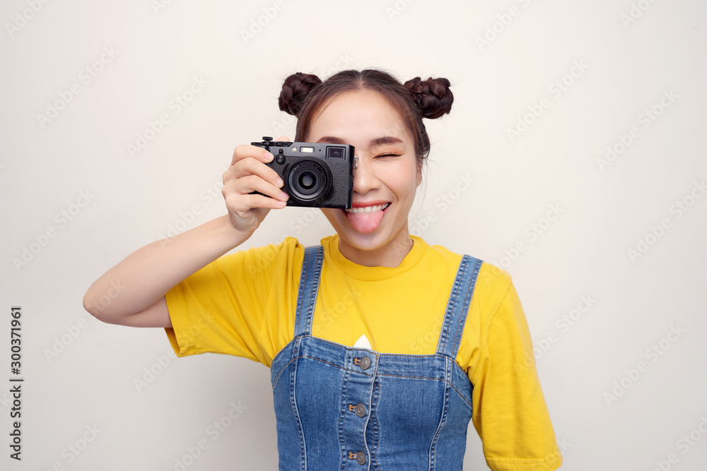 Beautiful woman, with top knot hairdo, wearing on denim jumpsuit, is holding retro camera like she i