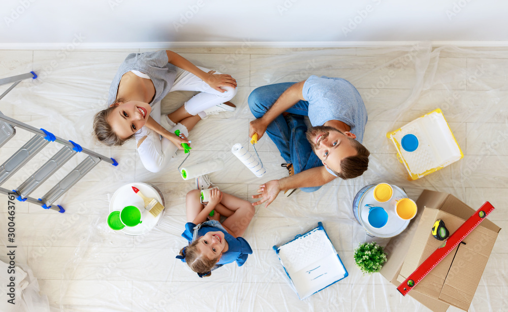 Repair in apartment. Happy family mother, father and child daughter  paints wall