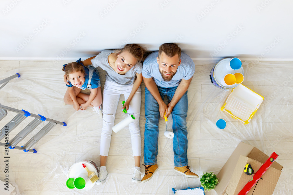 Repair in apartment. Happy family mother, father and child daughter  paints wall .