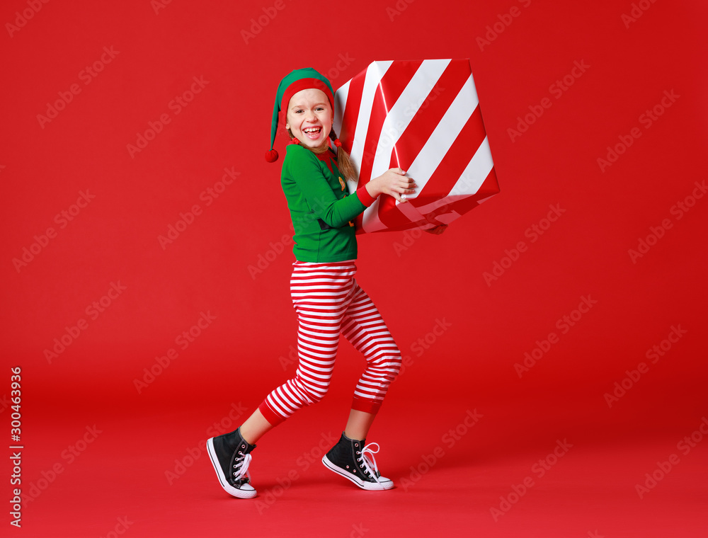 cheerful funny baby in Christmas elf costume with gifts on   red background.