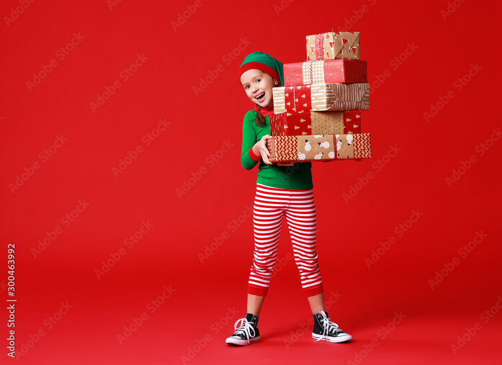 cheerful funny baby in Christmas elf costume with gifts on   red background.