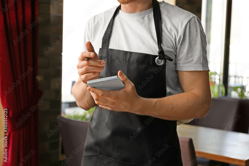 餐厅里拿着笔记本的年轻男服务员，特写