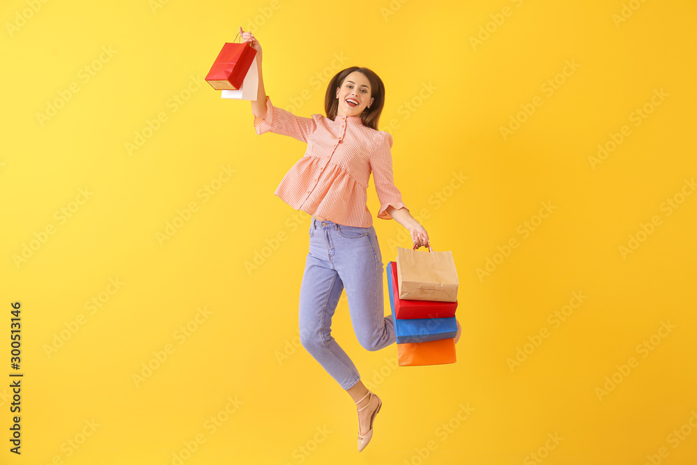 Happy jumping young woman with shopping bags on color background