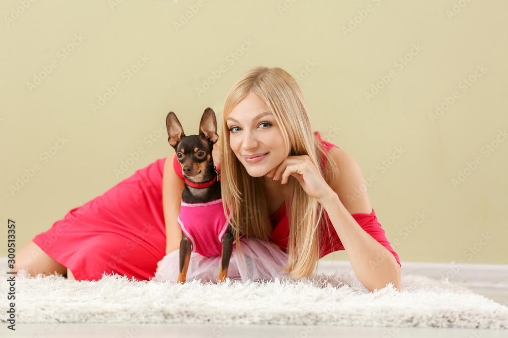 Fashionable young woman with cute toy terrier dog against color wall