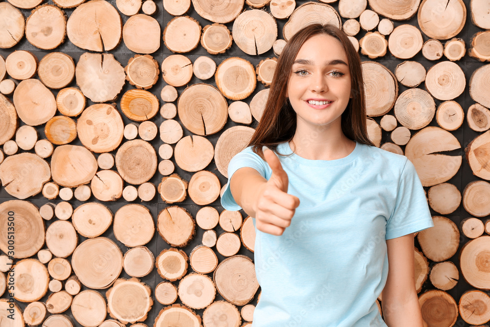 Beautiful teenage girl showing thumb-up on wooden background