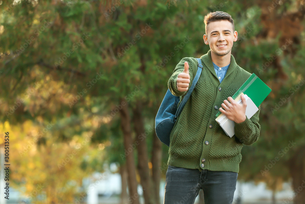 Portrait of teenage male student showing thumb-up outdoors