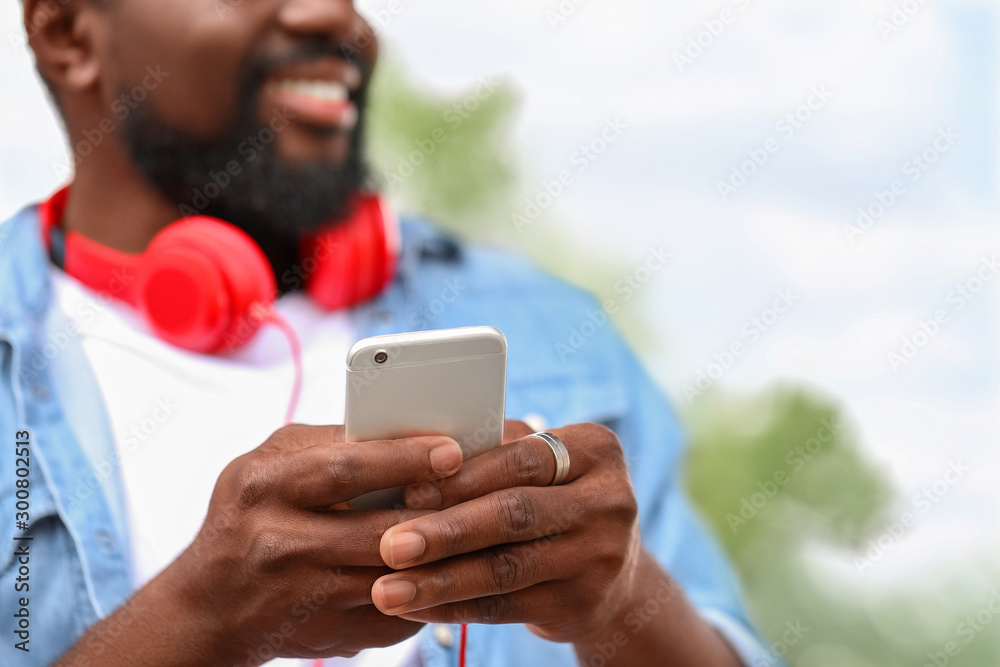 Handsome African-American man with mobile phone and headphones outdoors