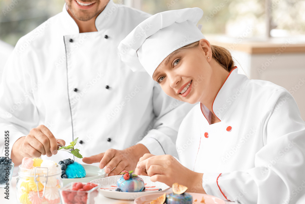 Young confectioners decorating tasty dessert in kitchen