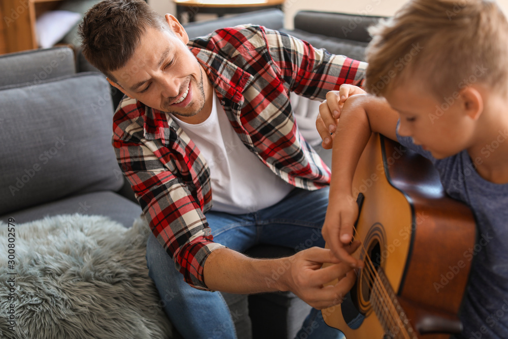 Father teaching his little son to play guitar at home