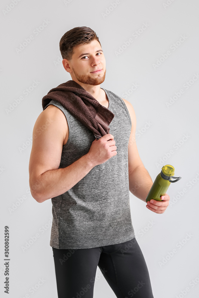 Sporty young man with bottle of water on light background