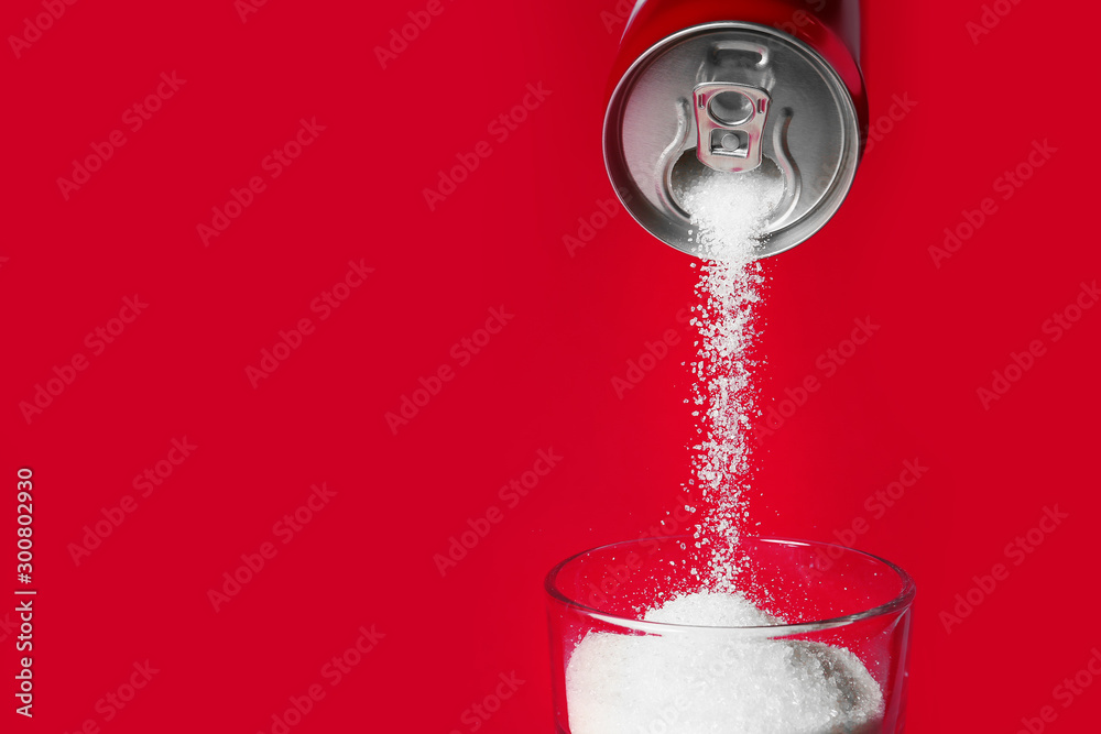 Pouring of sugar from can into glass on color background