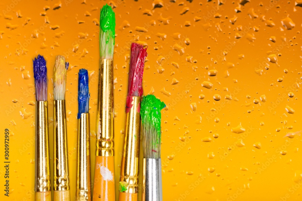 Artist paint brushes and paint cans of paint over bright watercolor background