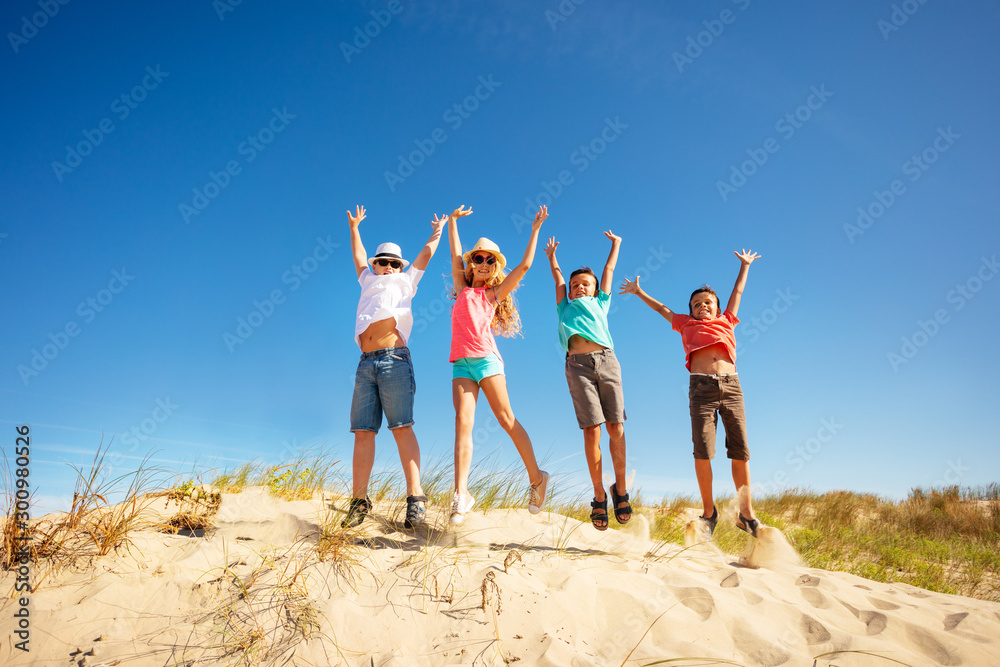 Happy cute children jump high up on the sand dune