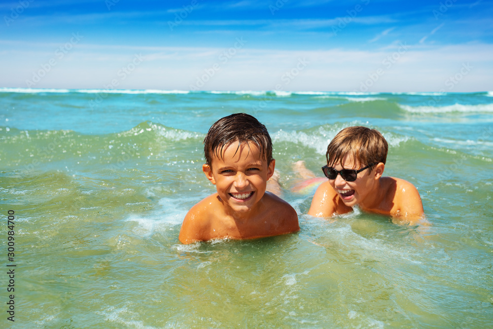 Two boys play in shallow water sea waves on beach