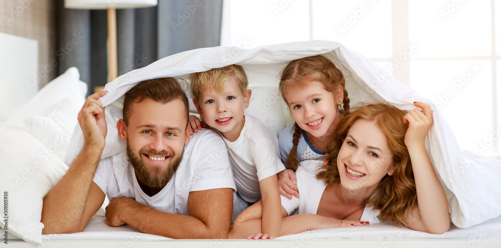 happy family mother, father and children laughing, playing and smiling in bed   at home.