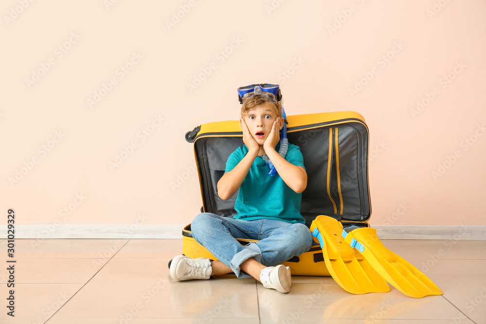 Surprised little boy sitting in suitcase near color wall