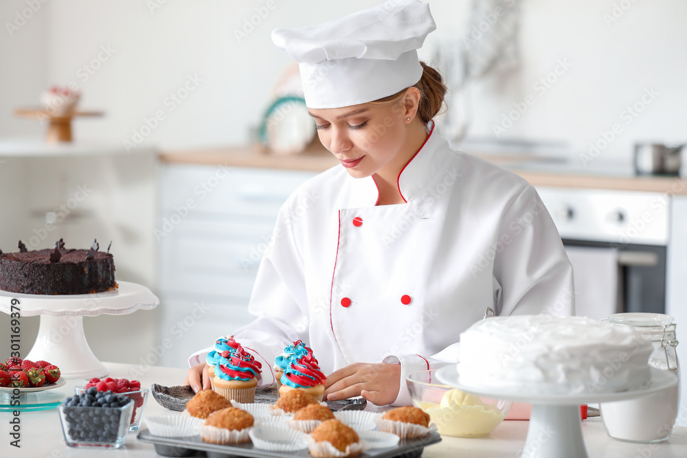 Female confectioner cooking tasty cupcakes in kitchen