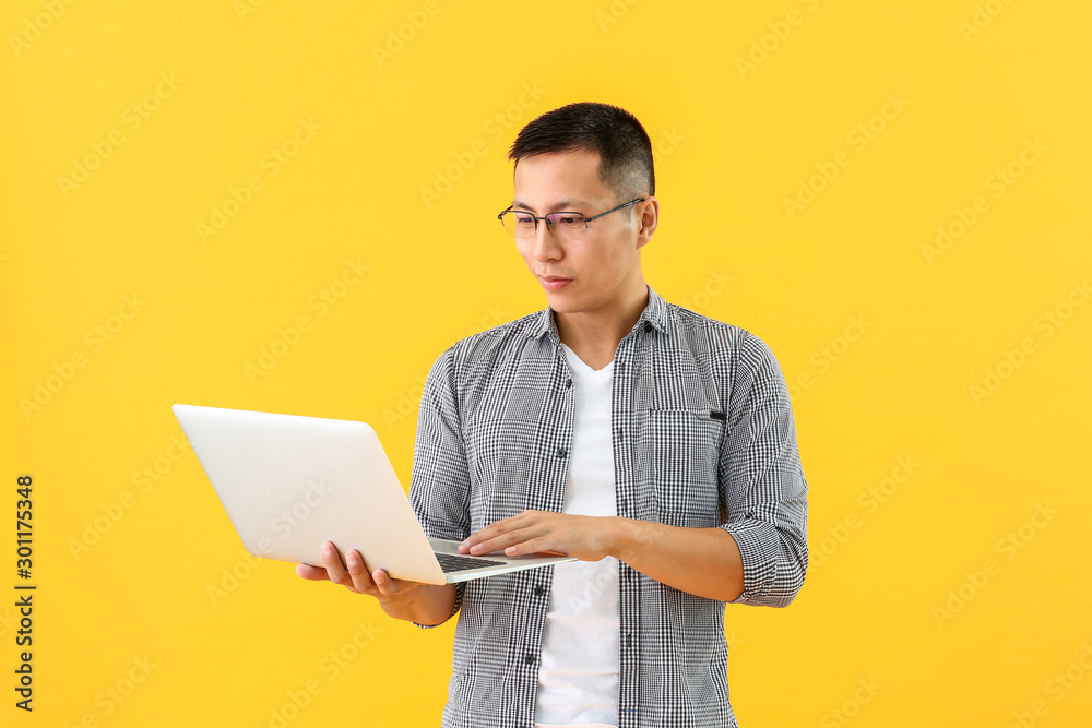 Male Asian programmer with laptop on color background