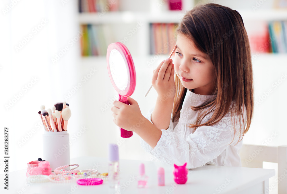 beautiful young girl, kid applying makeup with brush and pocket mirror