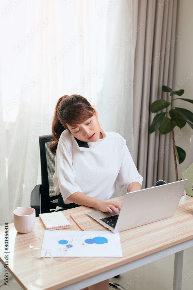 Young Asian woman using her cellphone while using laptop and working from home