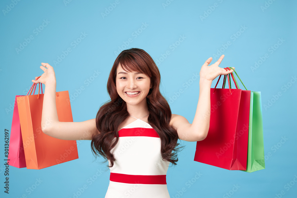 Beautiful young Asian woman with shopping bags on blue background