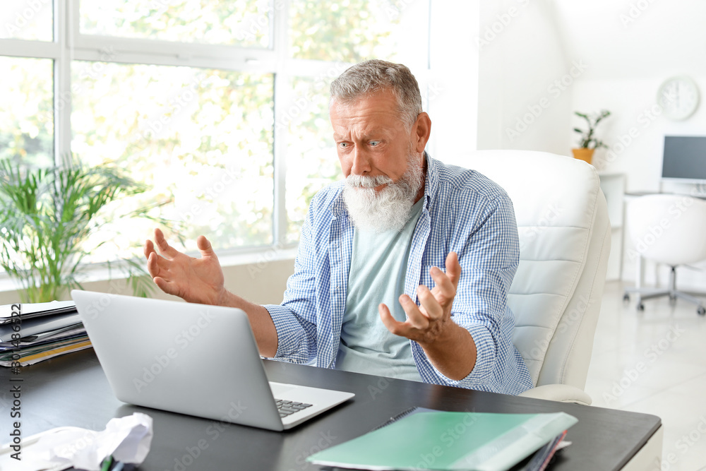 Angry mature man with laptop working in office