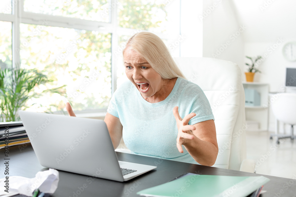 Angry mature woman with laptop working in office