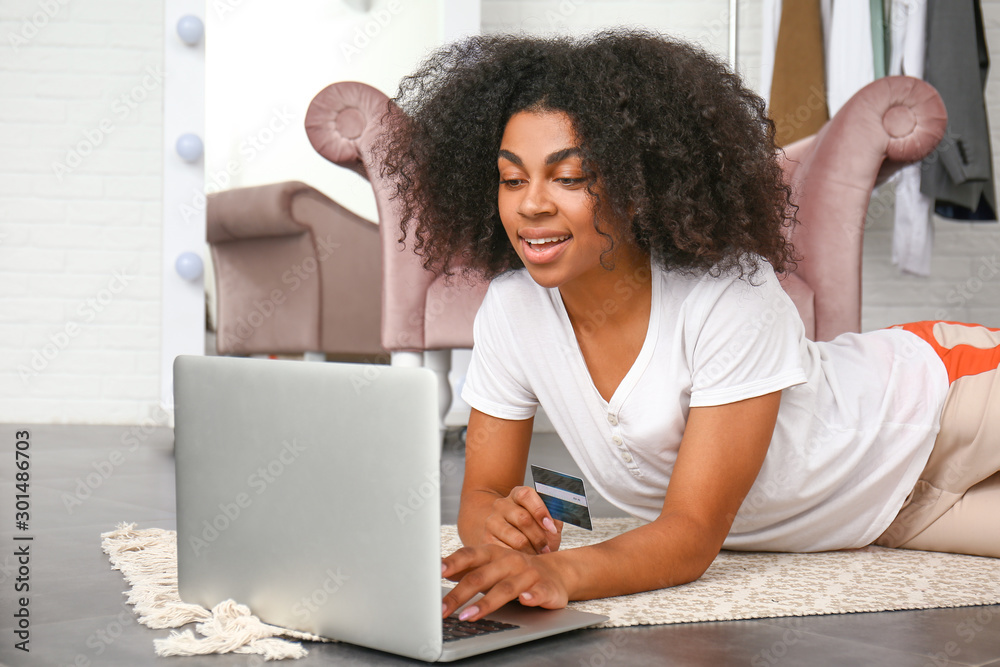 Beautiful African-American woman using laptop for online shopping at home