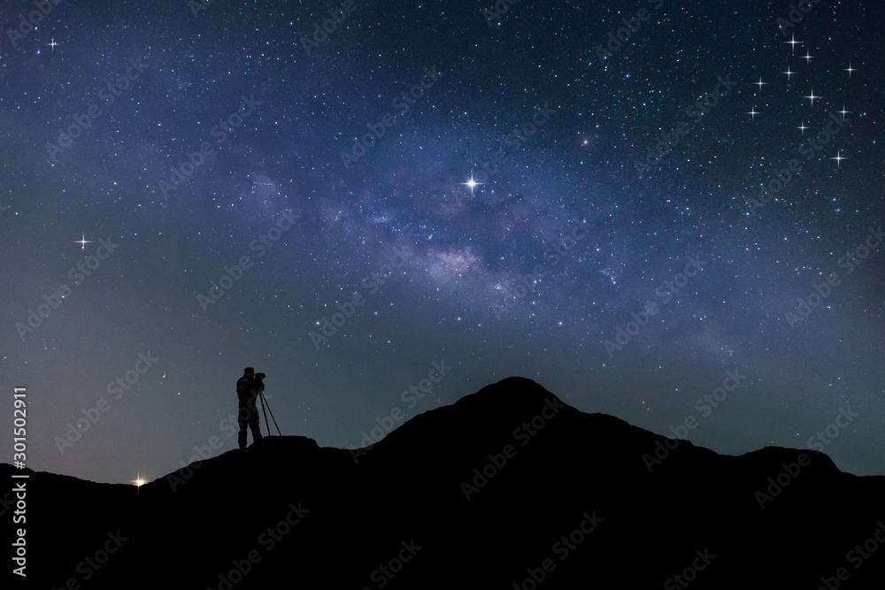 旅行者男人剪影站在山顶。全景蓝色夜空乳白色，星星在黑暗的背面。