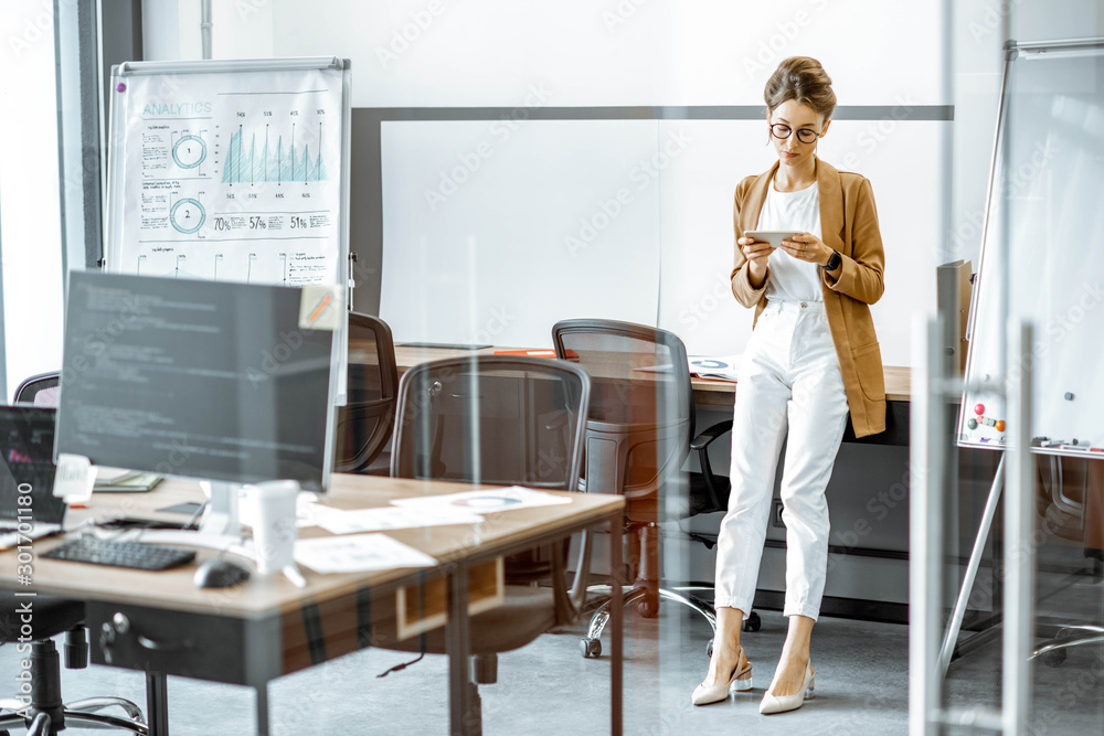 Young business woman preparing for a presentation, standing alone with phone near flipchart in the m