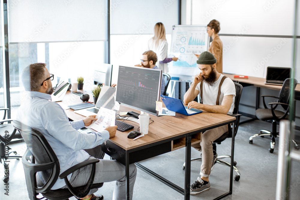 Group of diverse colleagues working on the computers in the modern office or coworking space, writin