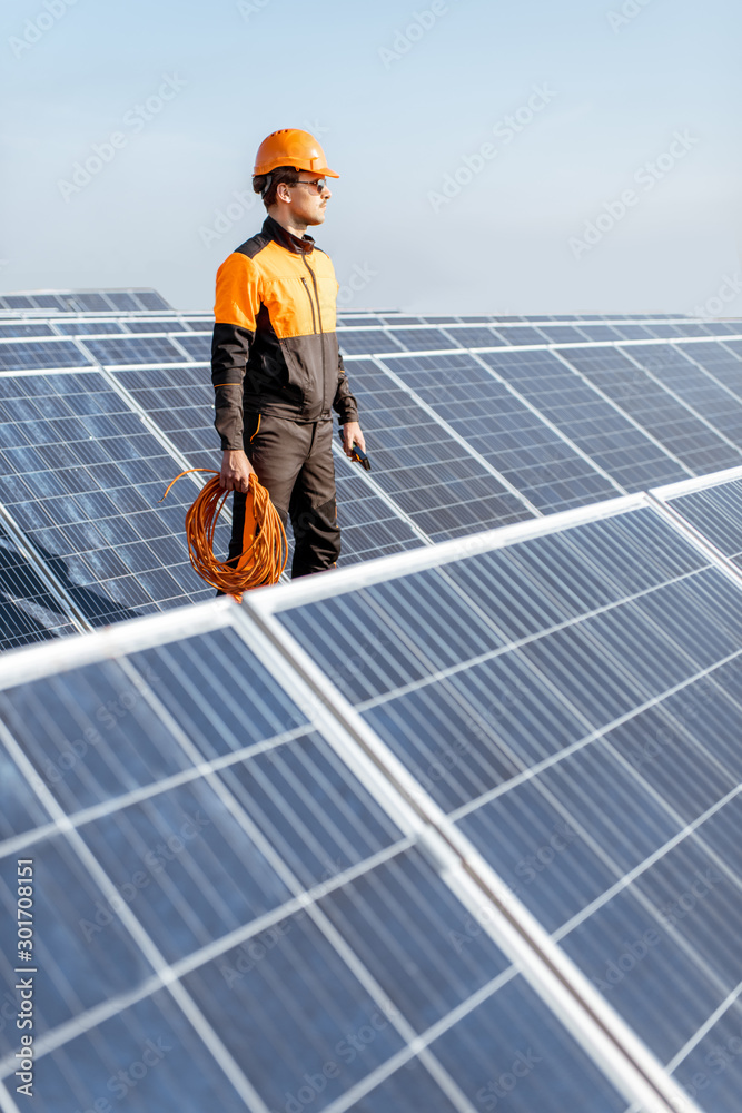 Well-equipped worker in protective orange clothing servicing solar panels on a photovoltaic rooftop 