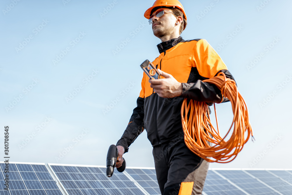 穿着橙色防护服的设备精良的工人在光伏屋顶上为太阳能电池板服务