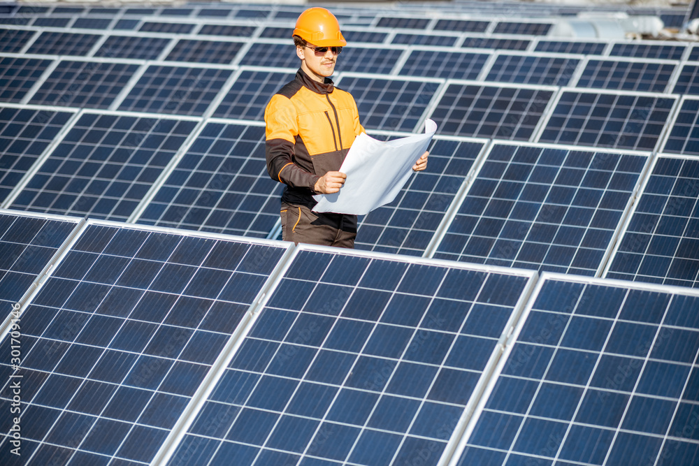 Engineer in protective workwear with blueprints of solar station project on a photovoltaic rooftop p