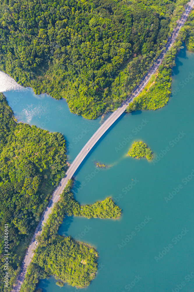 Top View of Rural Road from the drone , passing through the green forest and lake. Sunny day