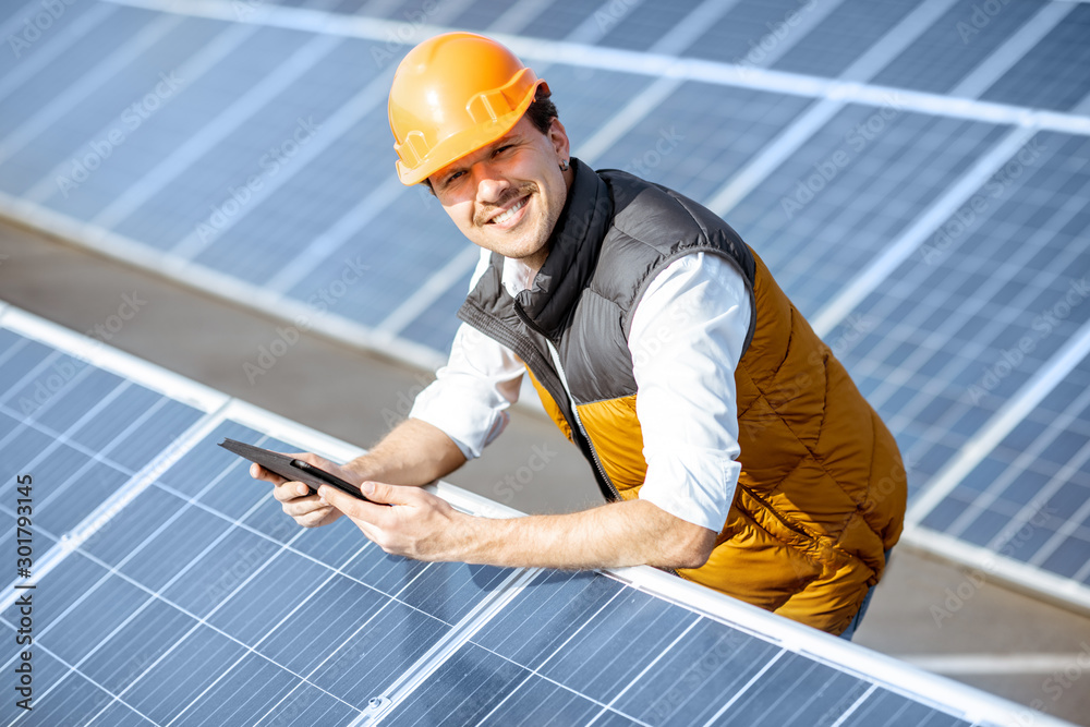 Portrait of a happy engineer in protective helmet standing with digital tablet on a solar power plan