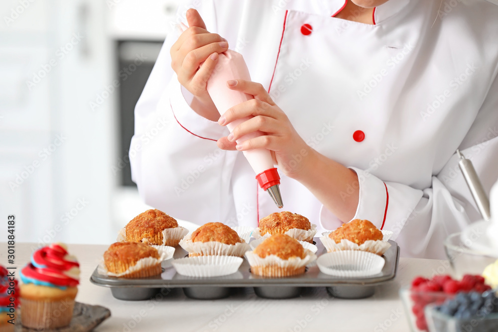 Female confectioner cooking tasty cupcakes in kitchen