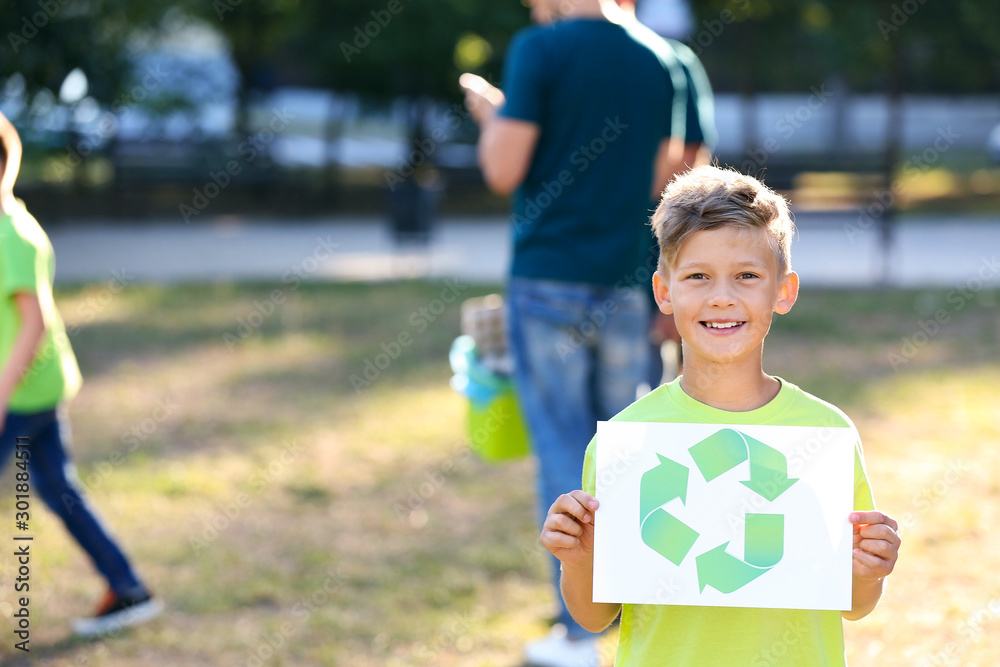 Boy holding paper sheet with symbol of recycling outdoors