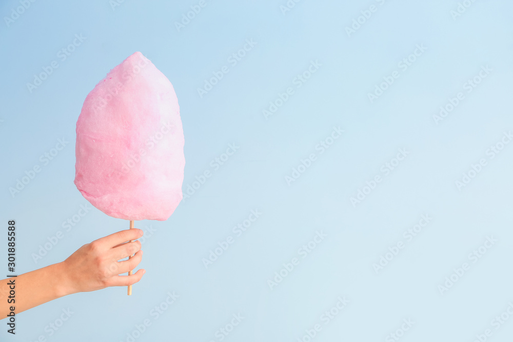 Female hand with tasty cotton candy on light background