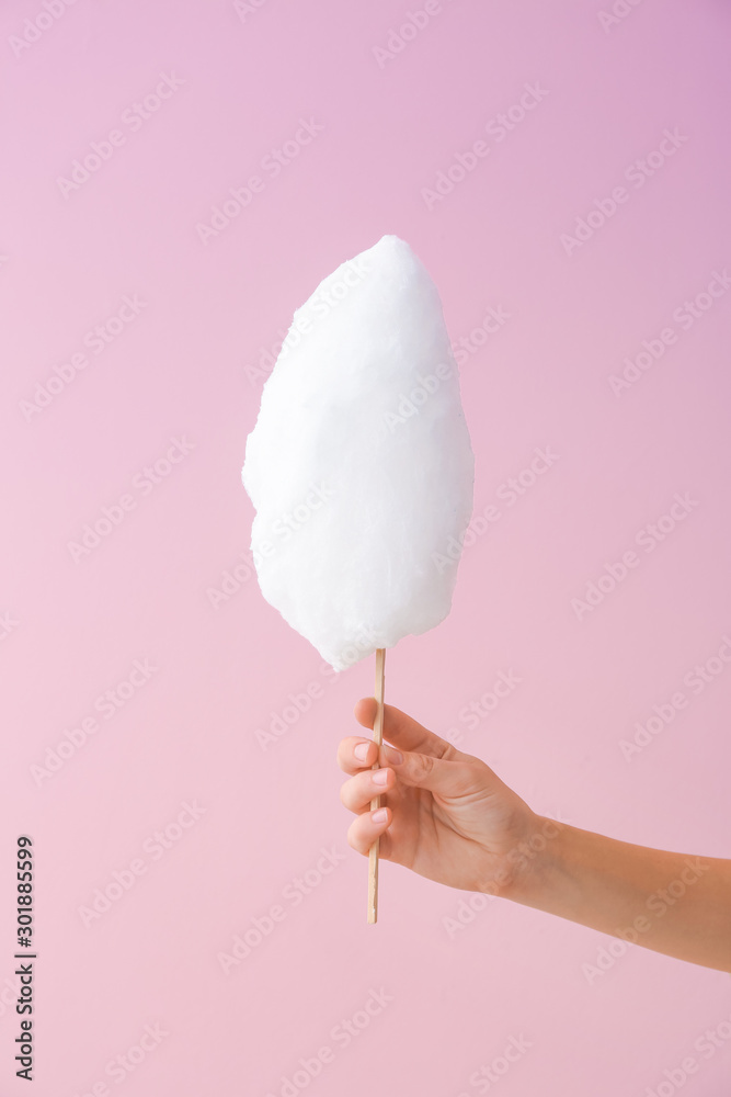 Female hand with tasty cotton candy on color background