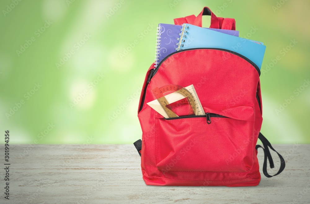 Open blue school backpack on wooden desk background.