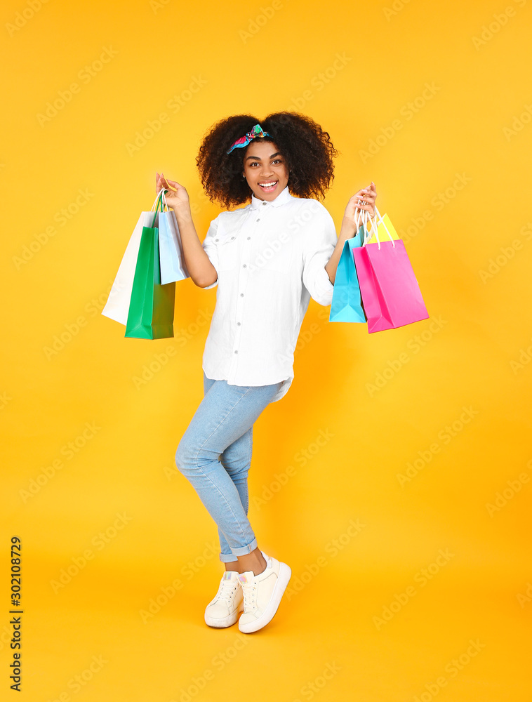 Beautiful African-American woman with shopping bags on color background