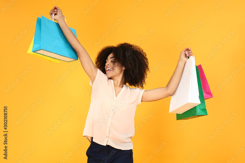 Beautiful African-American woman with shopping bags on color background