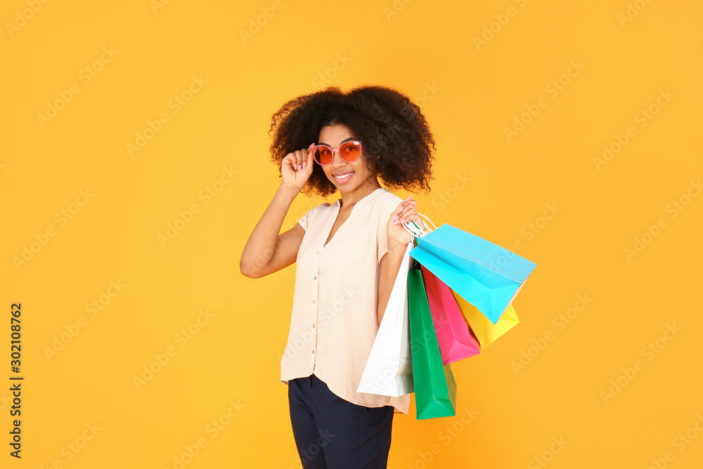 Beautiful African-American woman with shopping bags on color background