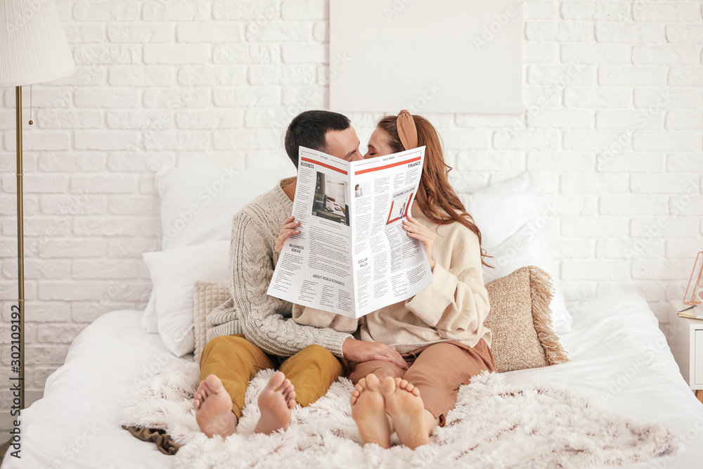 Beautiful young couple reading newspaper on bed at home