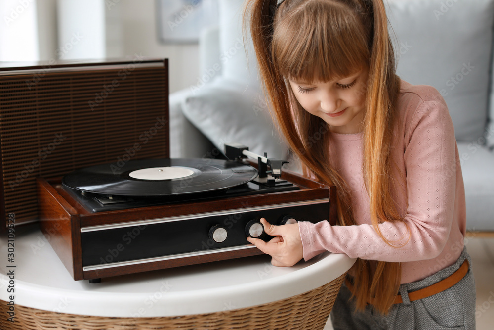 Cute little girl listening to music through record player at home